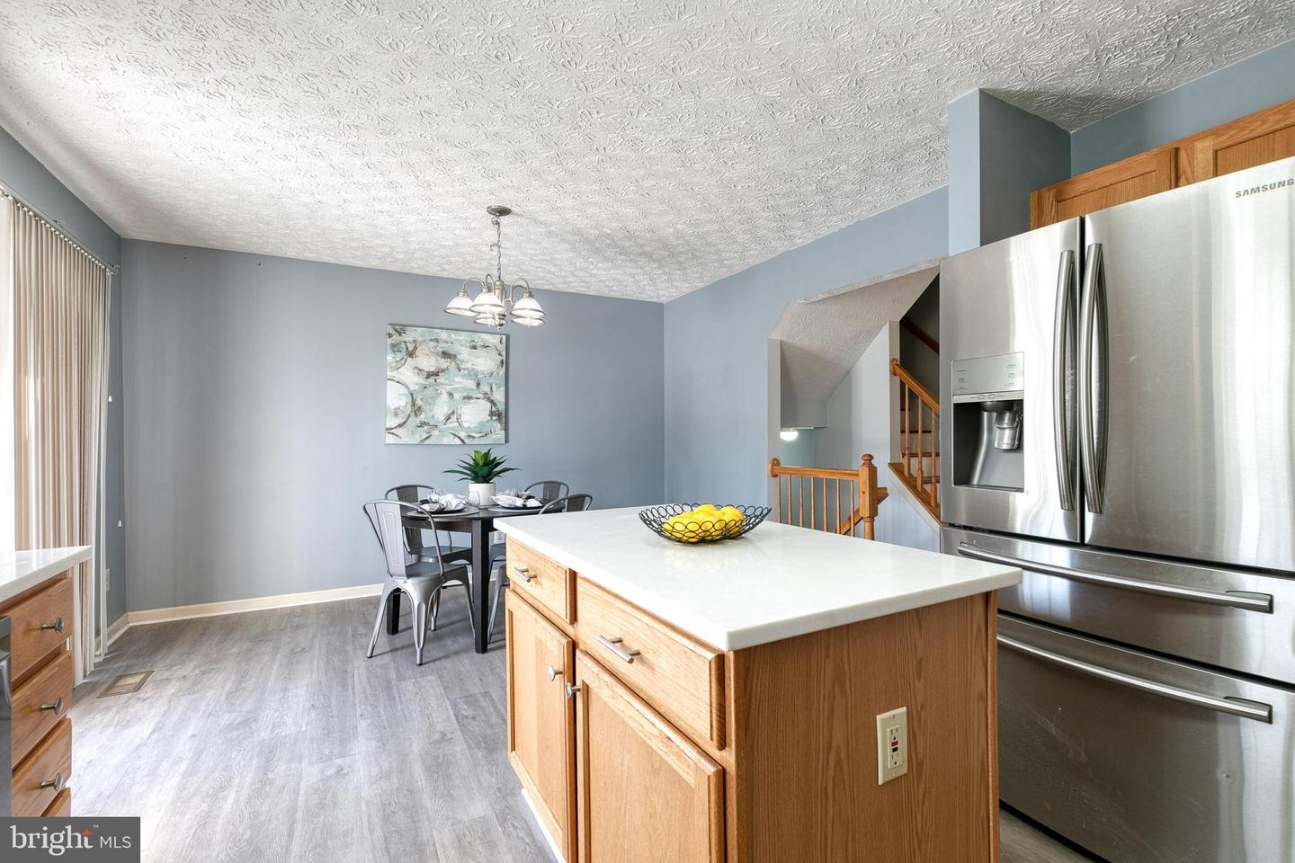 Kitchen with a white-topped wood island, stainless steel refrigerator, and dining area beside the staircase.
