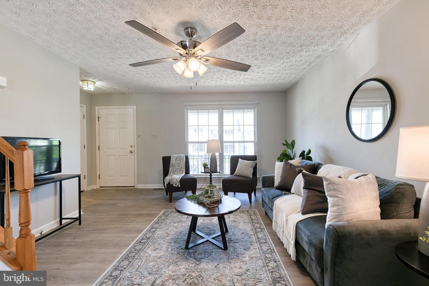 Living room with a gray sofa, patterned rug, ceiling fan, and large window.