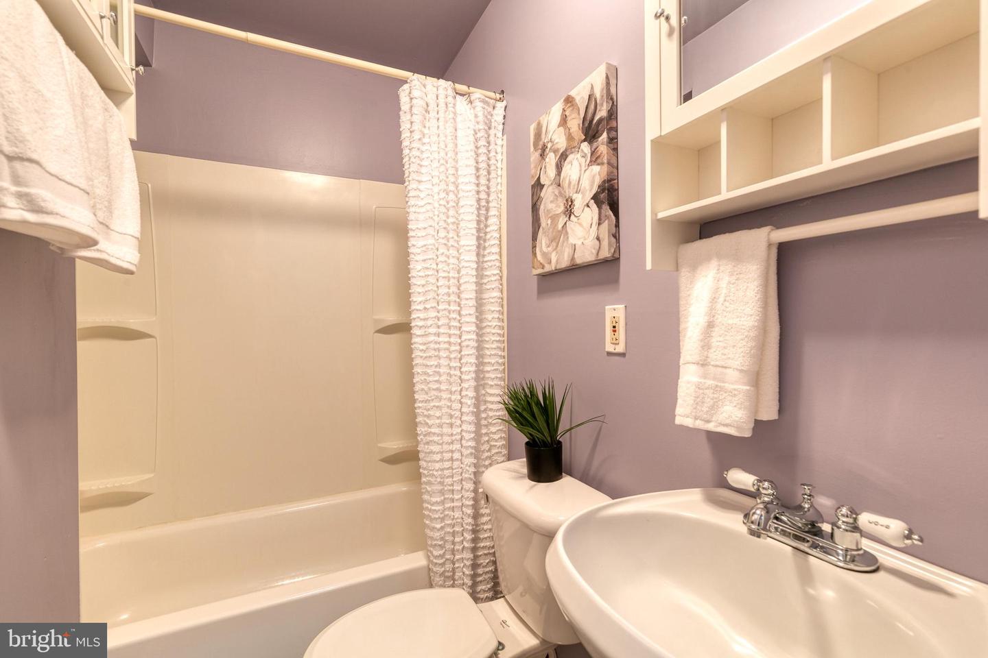 Bathroom with a white tub, textured shower curtain, lavender walls, and oval sink.