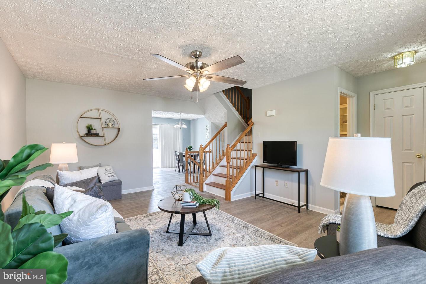 Living room with gray sofas, patterned rug, and a wooden staircase leading to the dining area.