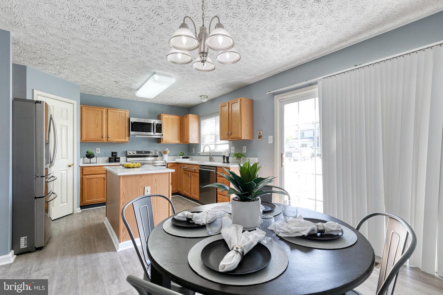 Kitchen with a central island and stainless steel appliances, opening to a dining area set for three.