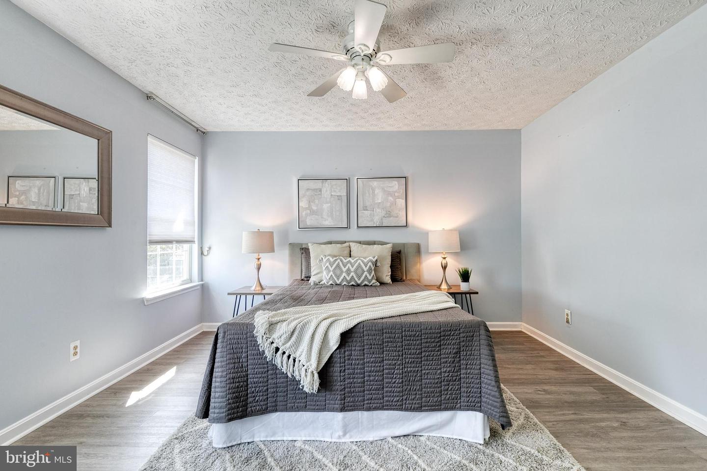 Staged bedroom with a gray-covered bed, white throw, matching lamps, and ceiling fan.