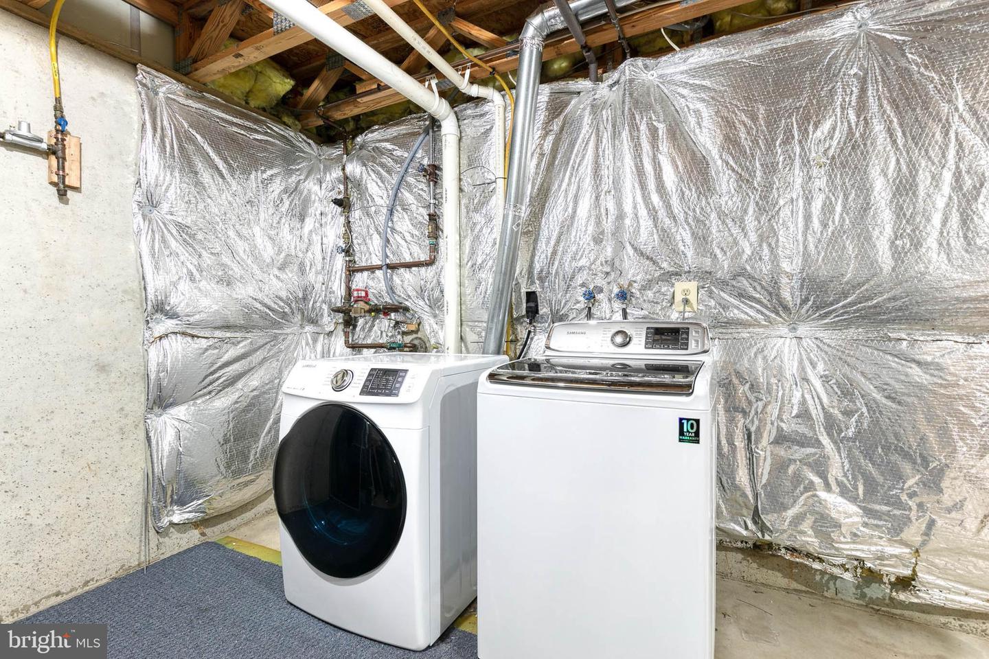 Basement laundry area with a front-load washer, top-load dryer, and reflective wall insulation.