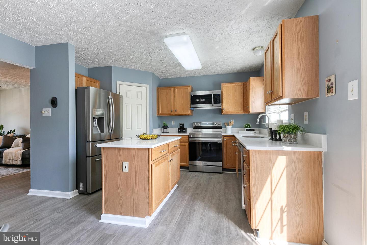 Kitchen with a central island, light wood cabinets, stainless steel appliances, and gray flooring.