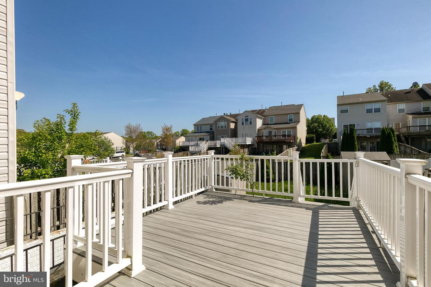 Deck with white railings overlooking neighboring homes, with sunlight casting long shadows across the gray planks.
