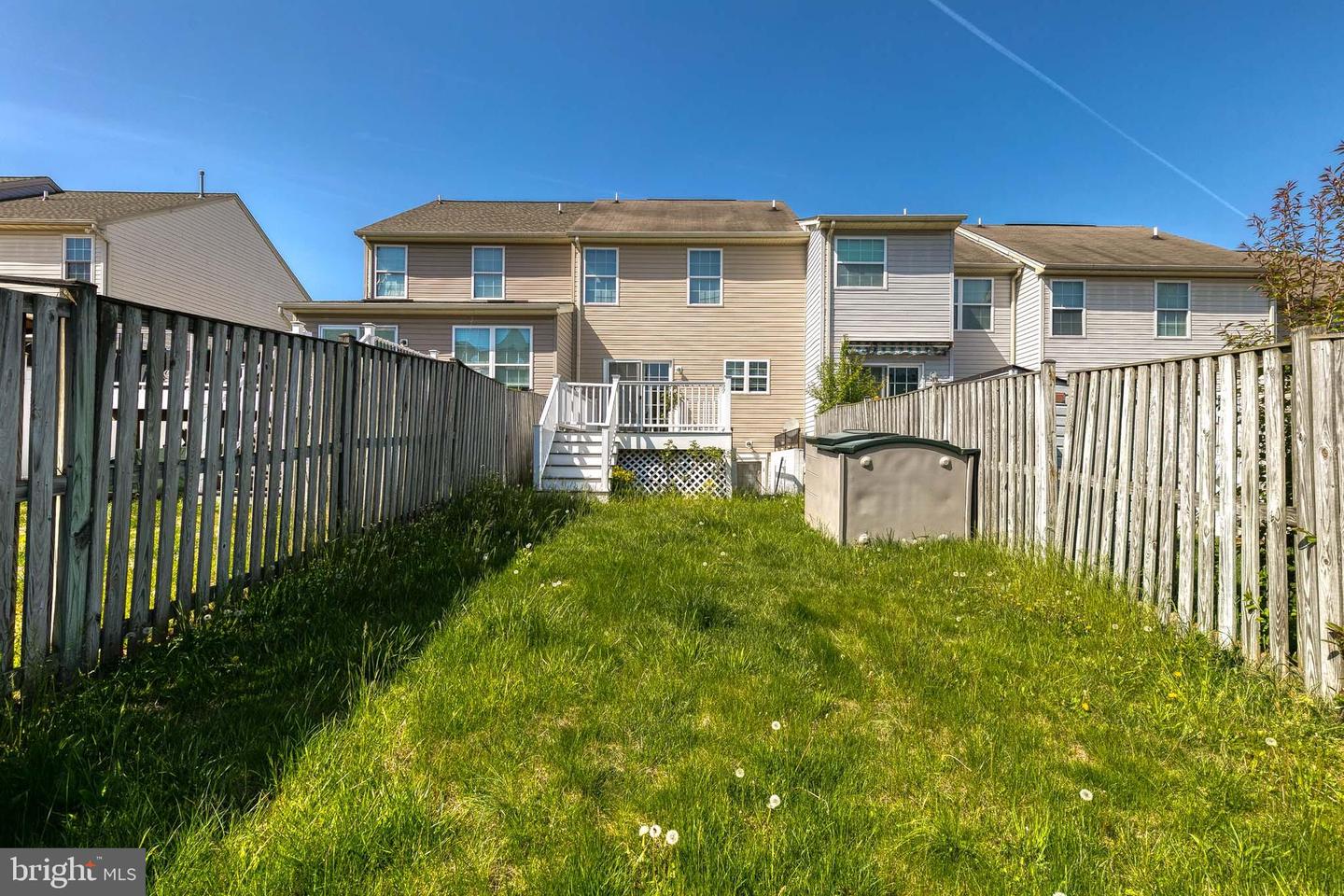 Townhouse rear and white deck stairs beyond a fenced, grassy backyard.