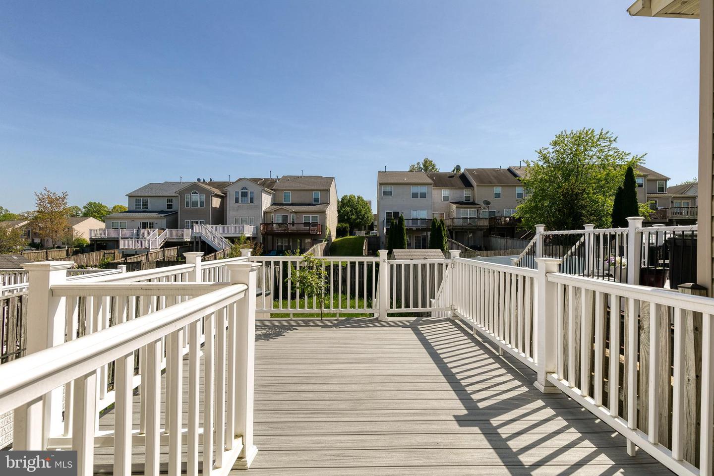 Elevated gray deck with white railings overlooking neighboring homes and trees.