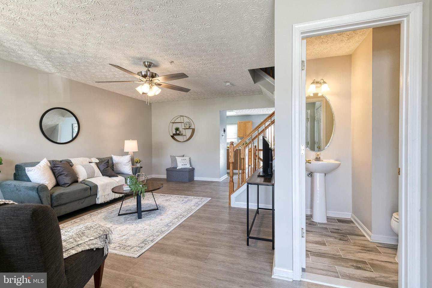 Staged living room with gray sectional and area rug, viewed beside an open powder room.