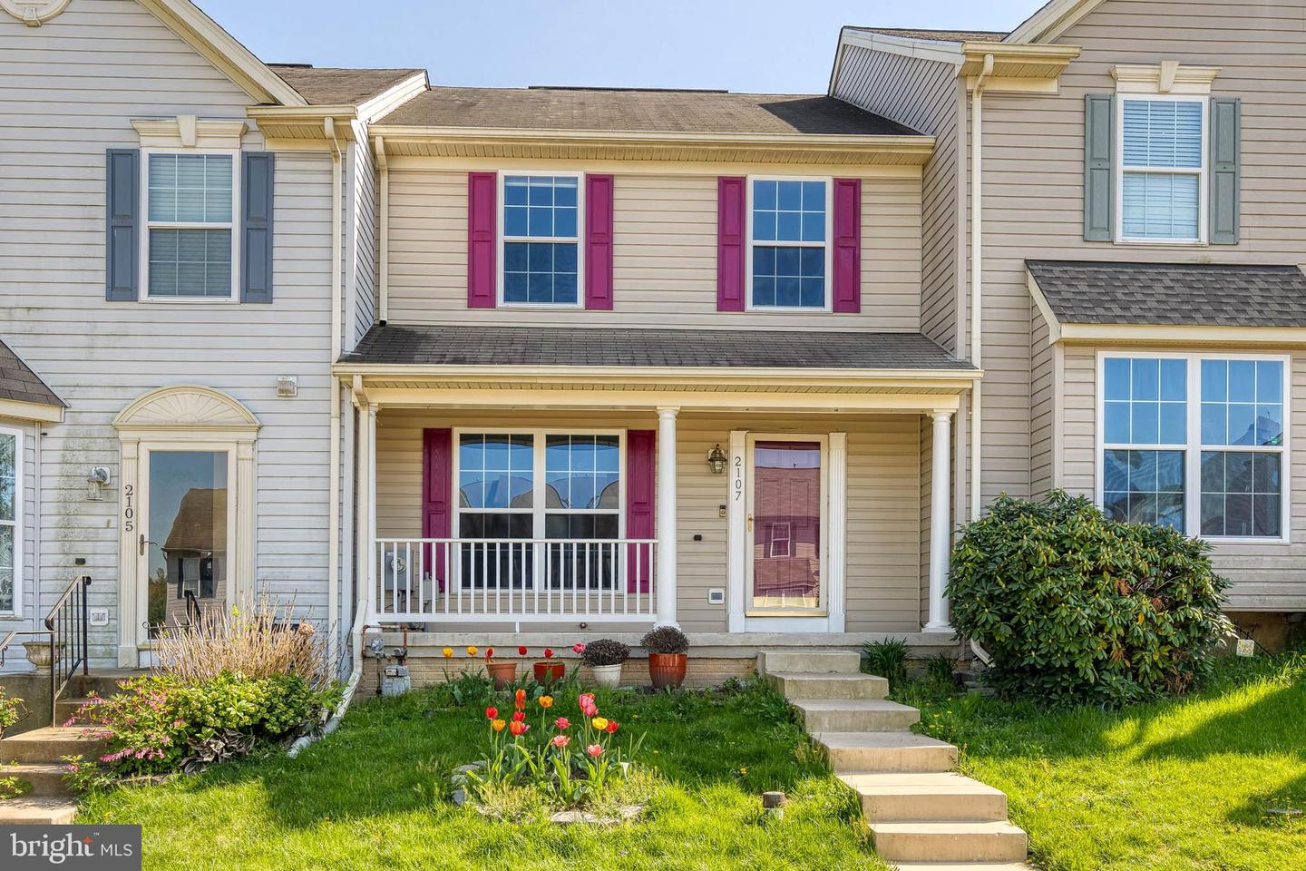 Townhouse front with burgundy shutters, a covered porch, and tulips beside the steps.