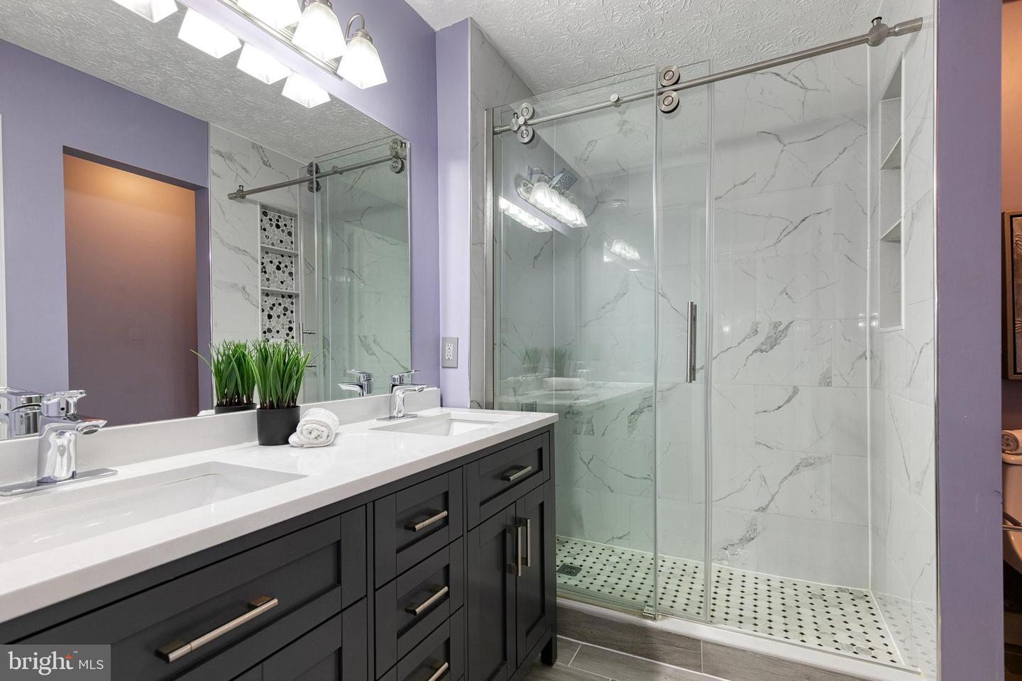 Bathroom with a dark double vanity and frameless glass shower featuring marble-look tile.