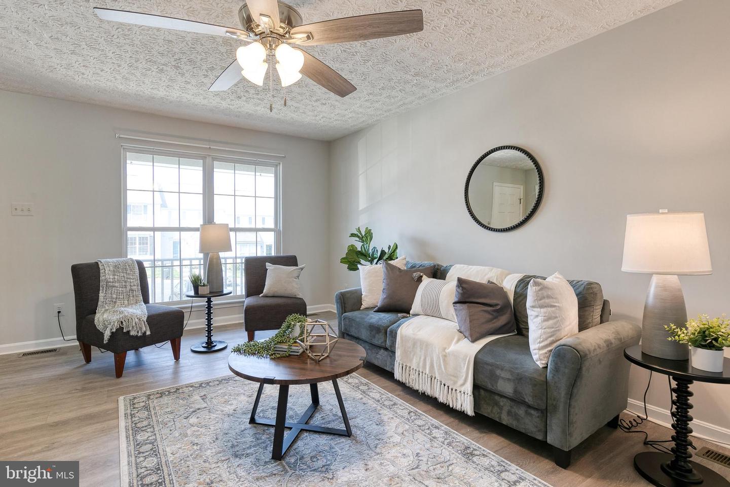 Staged living room with gray sofa, dark armchairs, patterned rug, and large window.