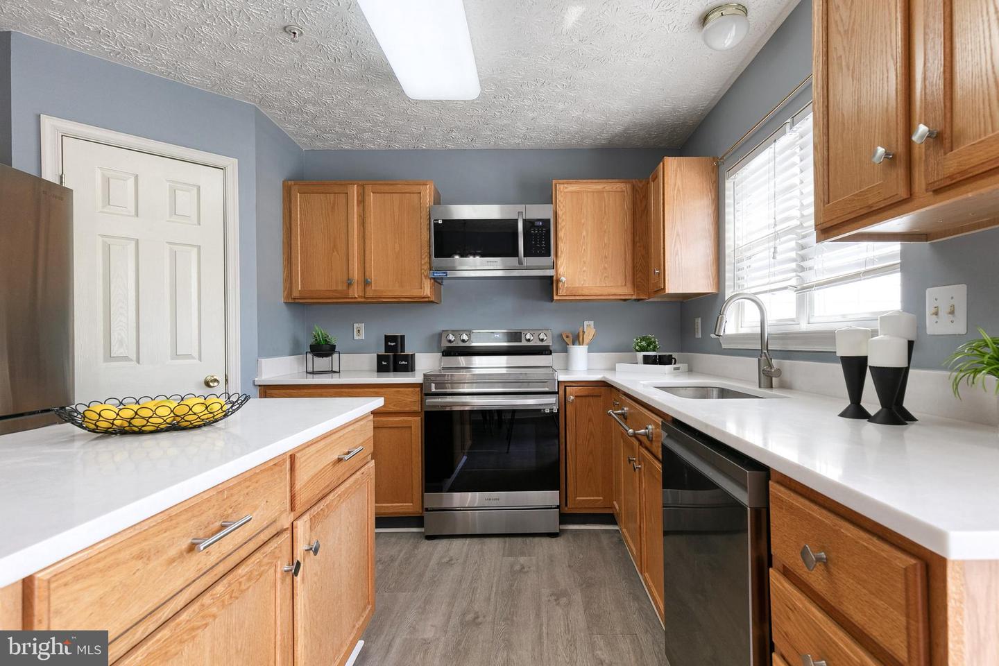 Kitchen with honey-colored cabinets, white countertops, stainless appliances, and a window above the sink.