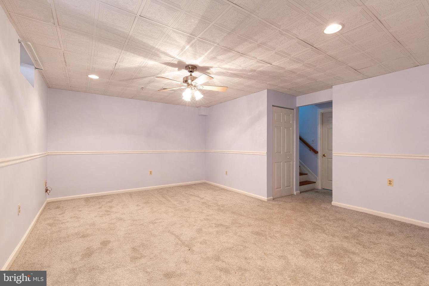 Empty carpeted room with a ceiling fan, patterned ceiling, and doorway to a stairwell.