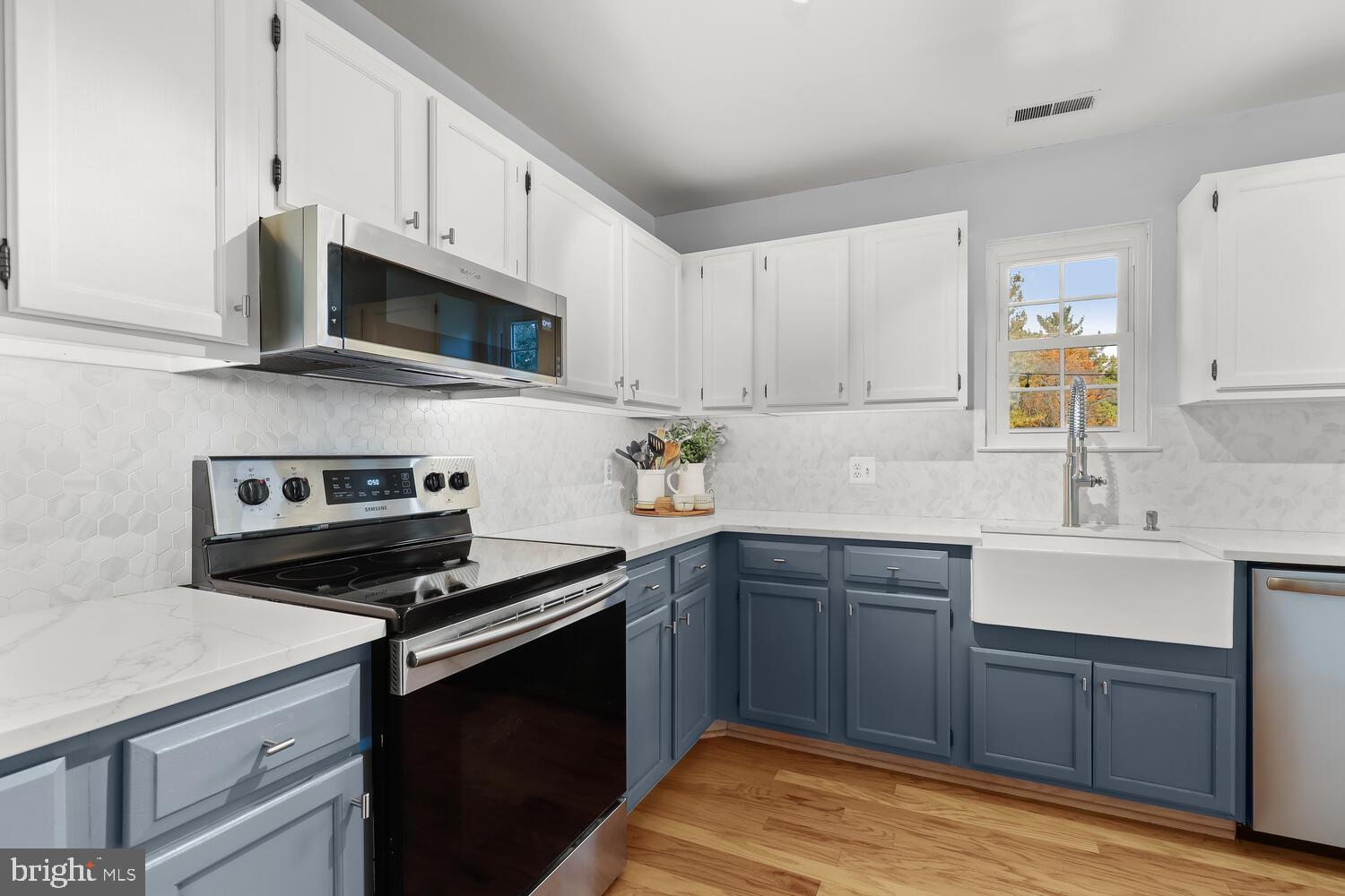 Kitchen with blue-gray lower cabinets, white counters, stainless appliances, and a farmhouse sink.