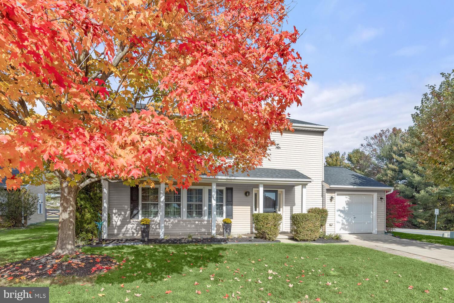 Two-story home with an attached garage and covered porch beneath a colorful autumn tree.