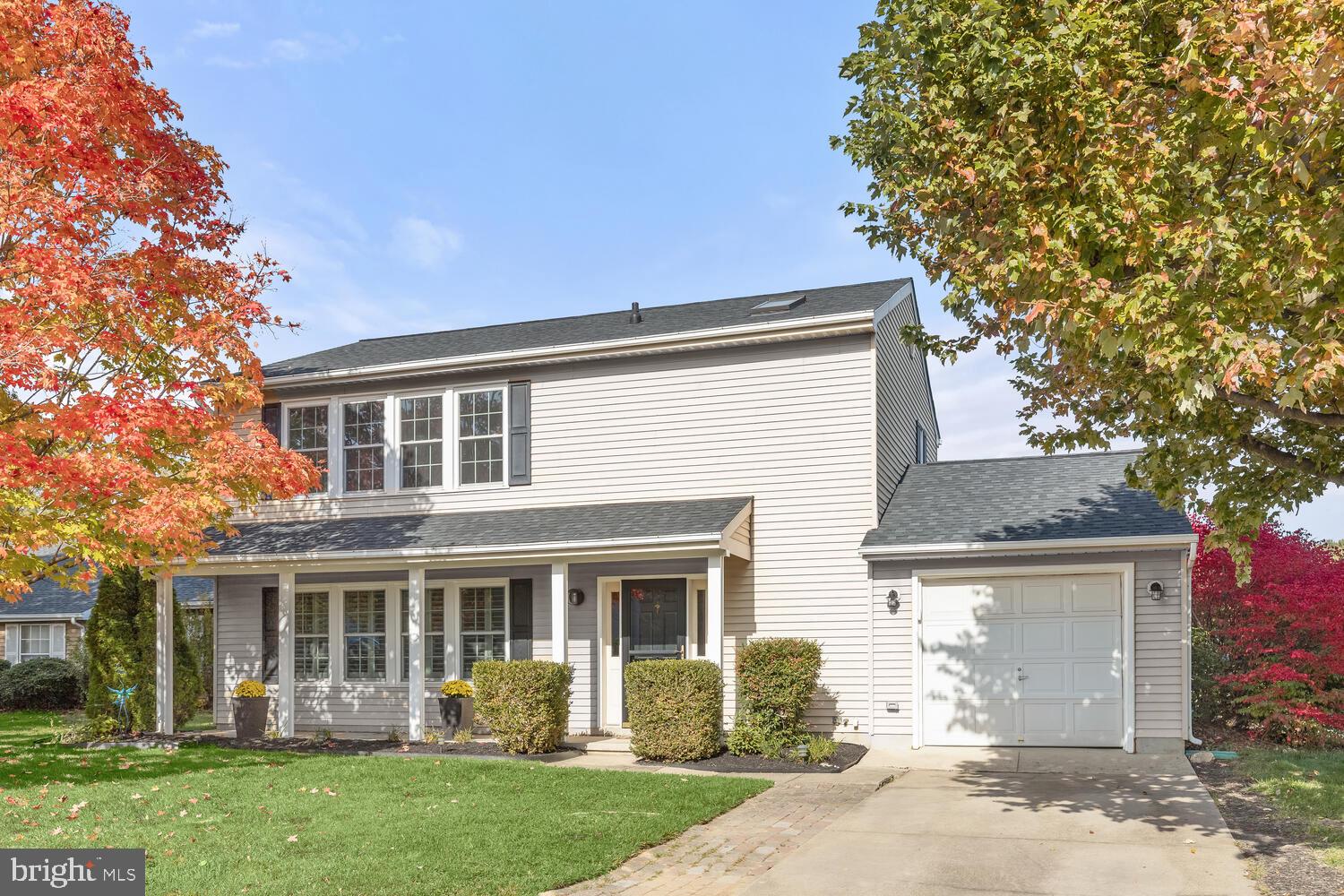 Two-story light-sided home with a covered porch and attached garage, framed by autumn trees.