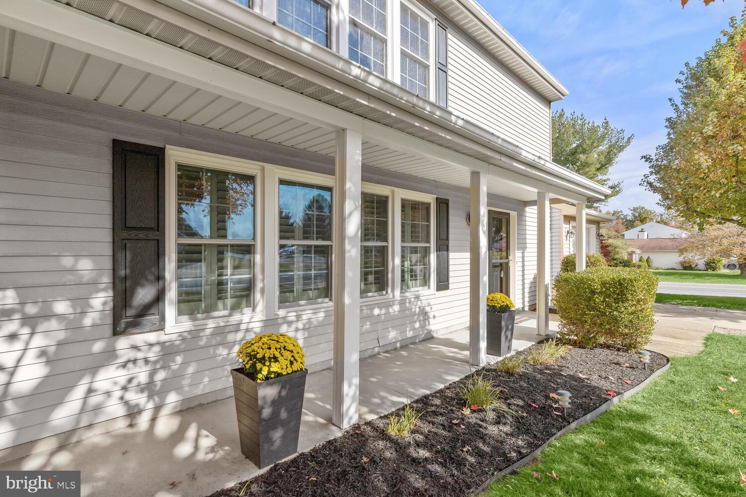 House exterior with a covered front porch, dark shutters, and yellow chrysanthemums in planters.