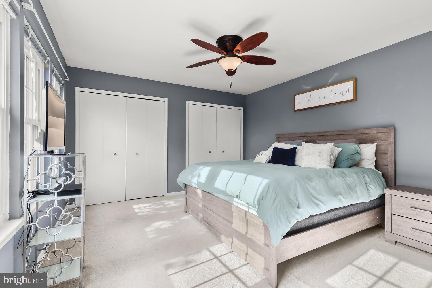 Bedroom with pale aqua bedding, a wood bed, two closets, and sunlight through tall windows.