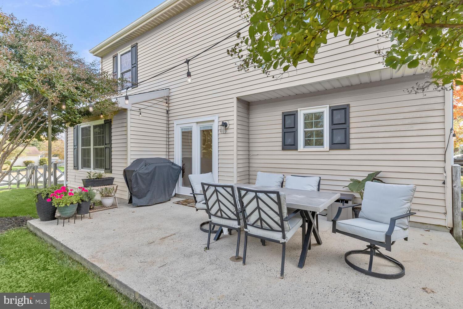 Backyard patio with an outdoor dining set, potted flowers, and a covered grill beside the home.
