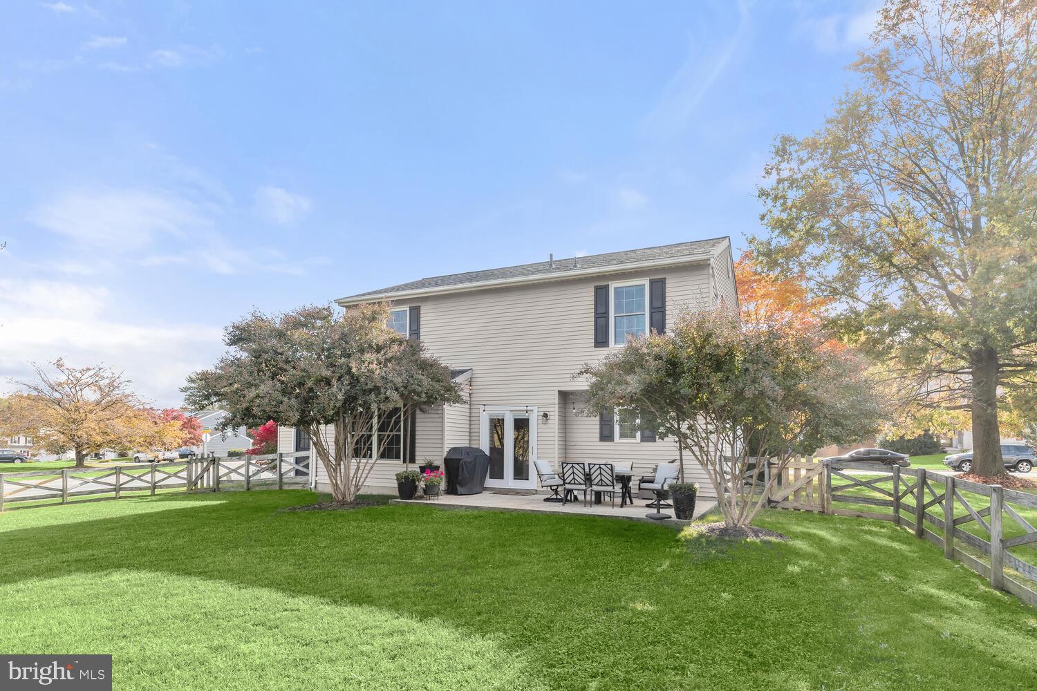 Two-story home with a fenced lawn and patio dining area beneath autumn trees.