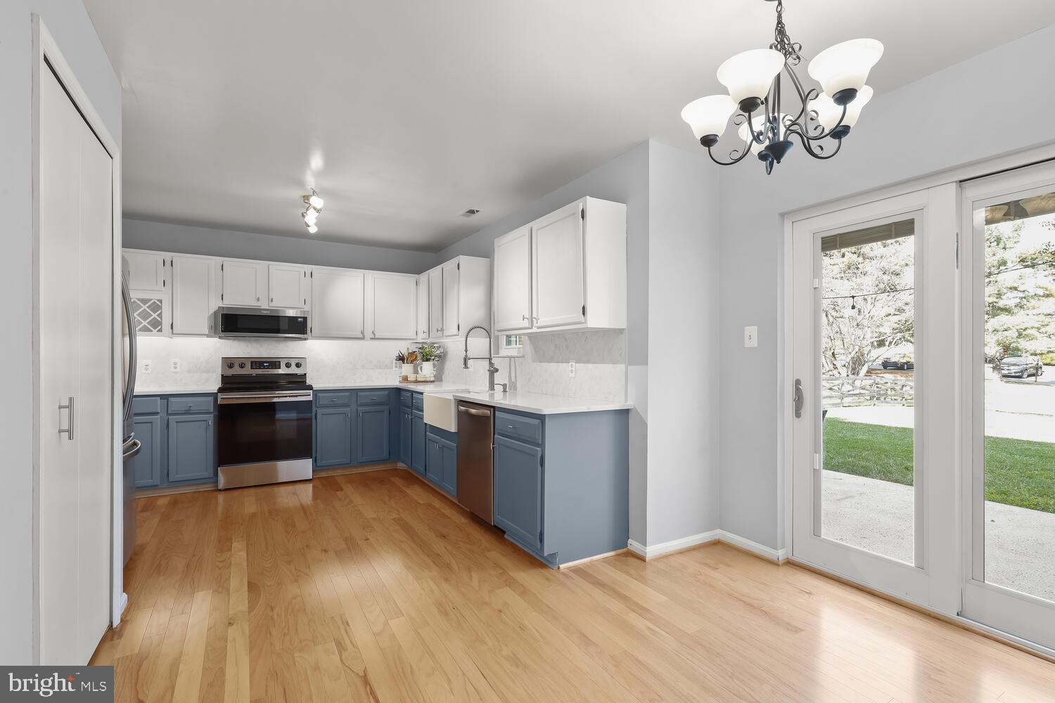 Kitchen with blue lower cabinets, white upper cabinets, farmhouse sink, and hardwood floors.