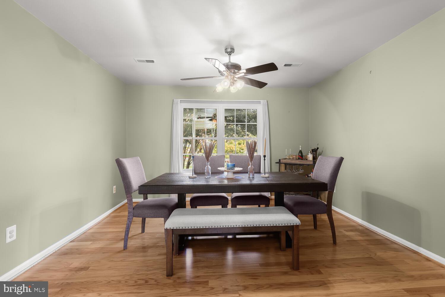 Dining room with a dark table, upholstered chairs, hardwood floors, and a large window.