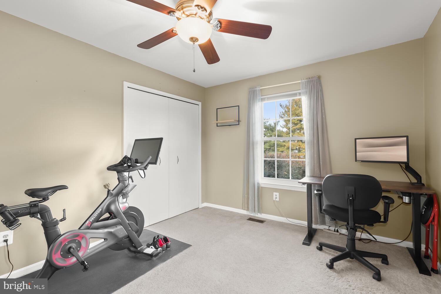 Home exercise room with a stationary bike beside a desk and window.