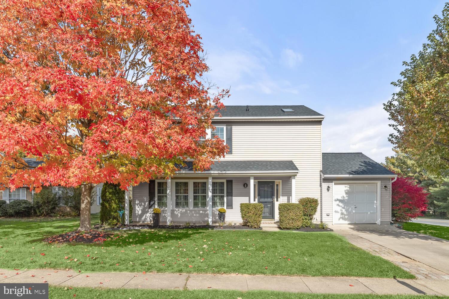 Two-story house with a covered porch and attached garage, framed by a red-orange autumn tree.