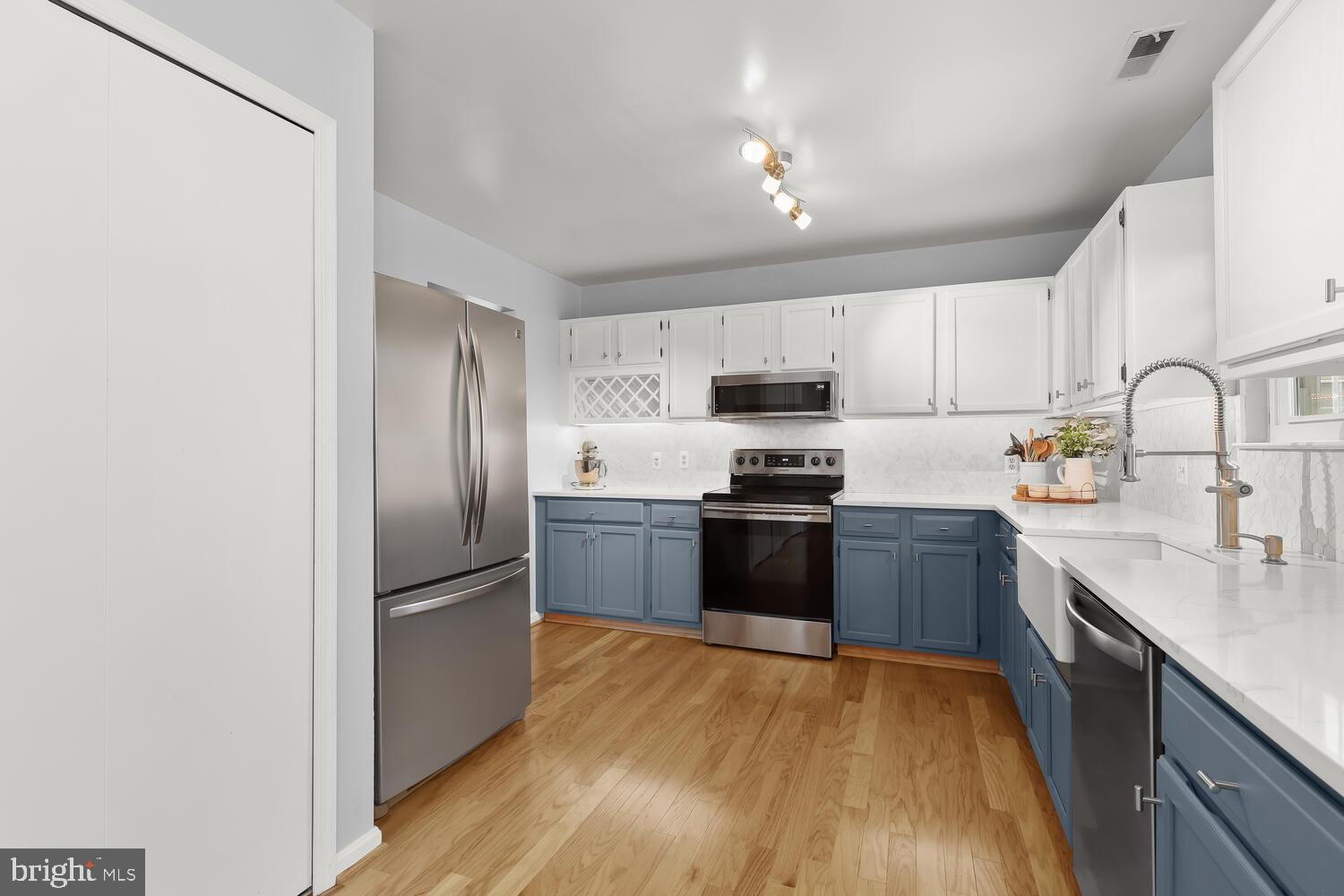 Kitchen with slate-blue lower cabinets, white countertops, and stainless steel appliances.