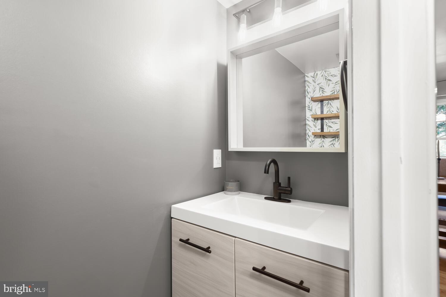 Bathroom vanity with a white sink, light wood drawers, black faucet, and large mirror.