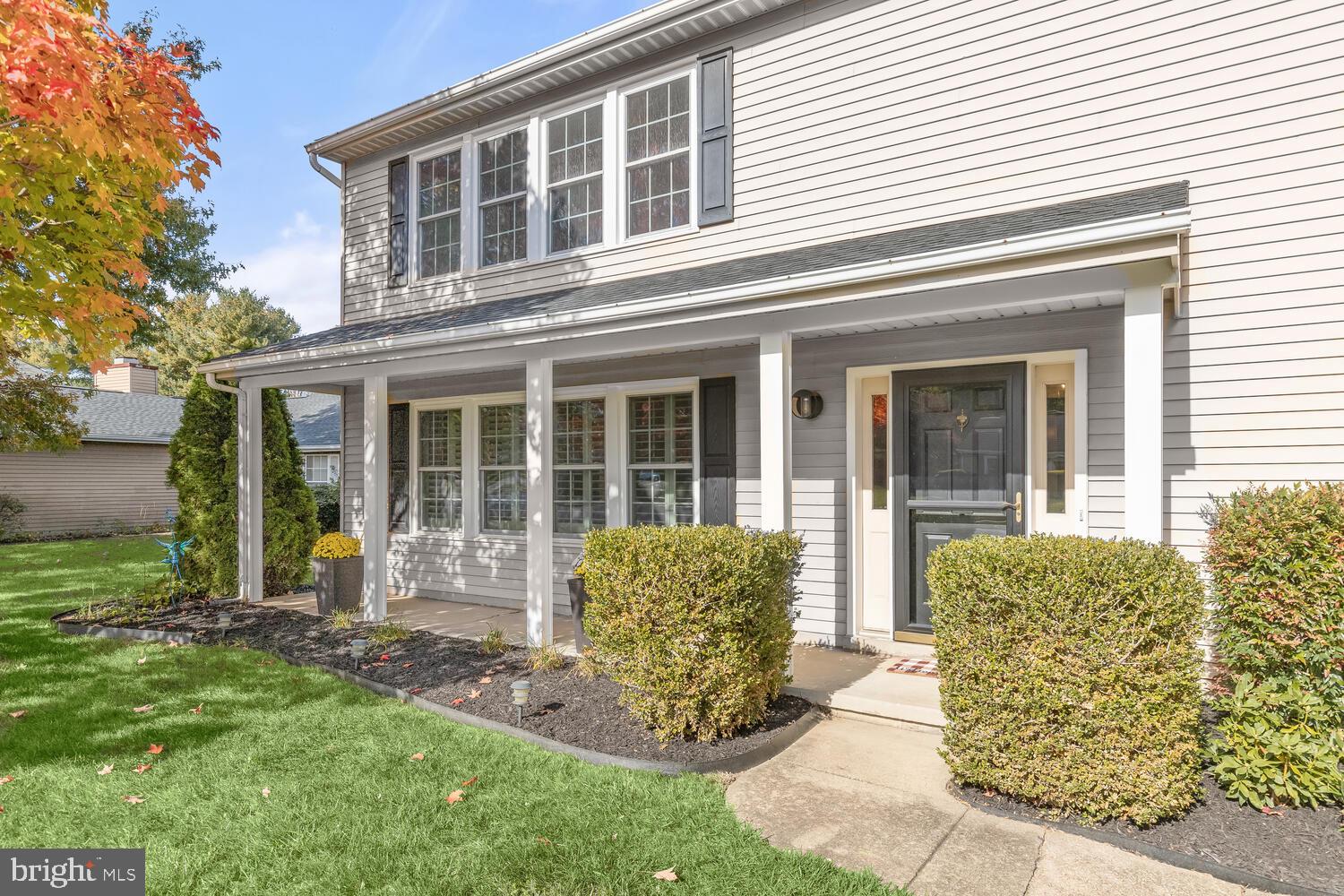 Two-story house with a covered front porch, dark entry door, and landscaped lawn.