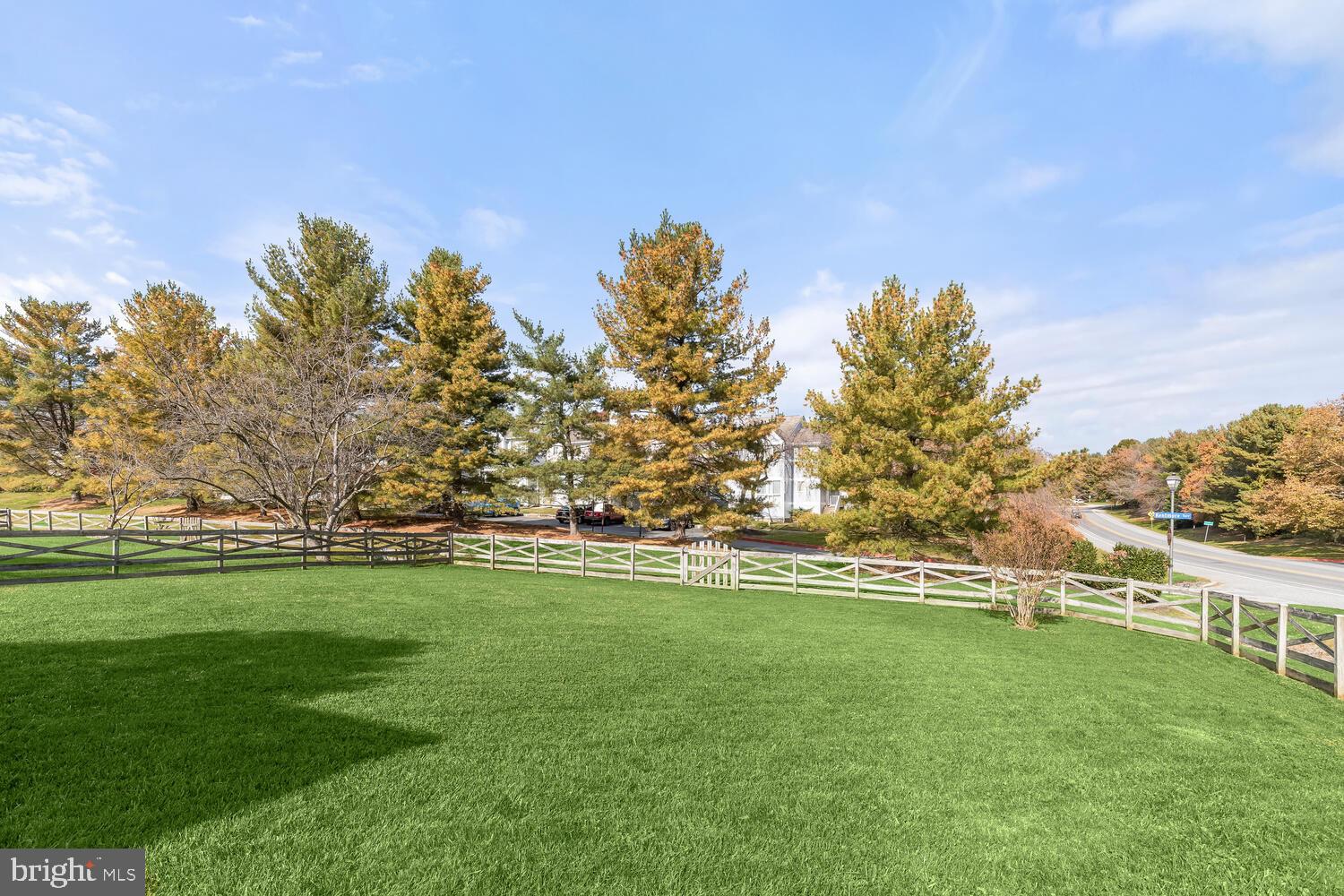 Broad lawn bordered by split-rail fencing, with autumn trees and the house partly visible beyond.