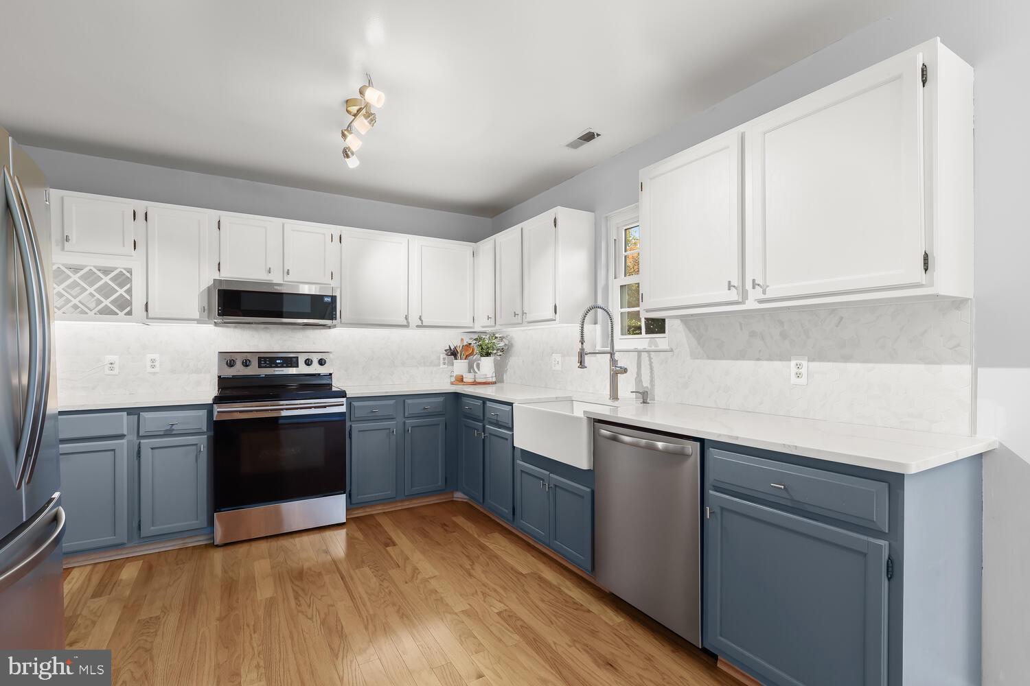 Kitchen with white upper cabinets, blue-gray lower cabinets, stainless appliances, and a farmhouse sink.
