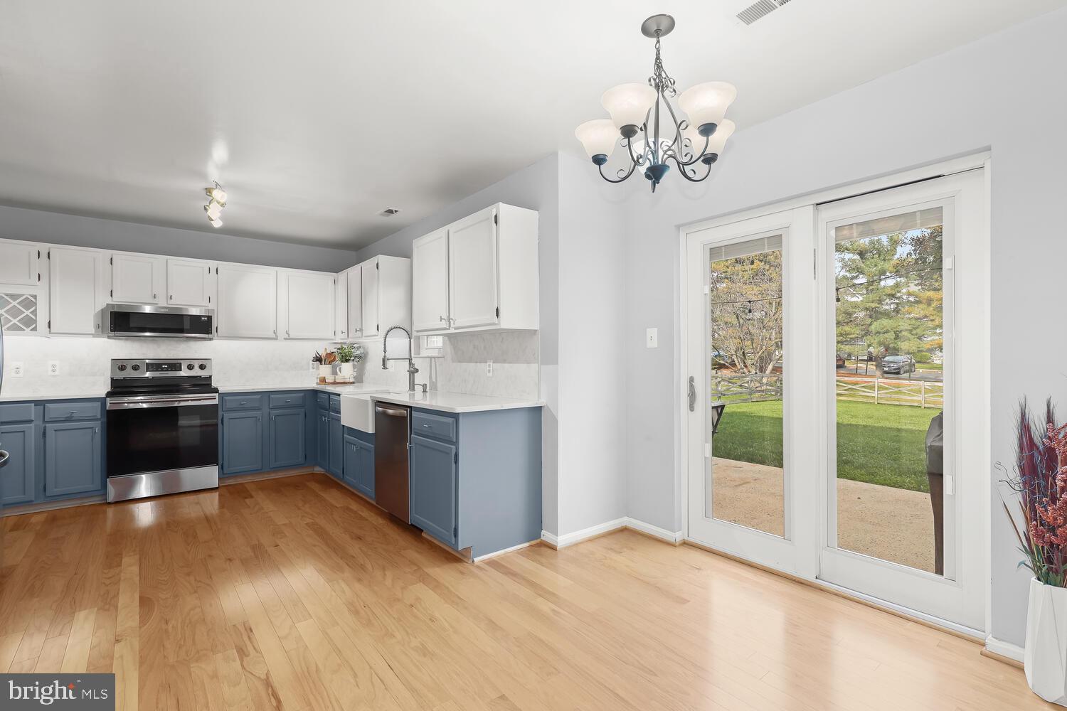 Kitchen with white and blue cabinets, stainless steel appliances, and glass patio doors to the backyard.