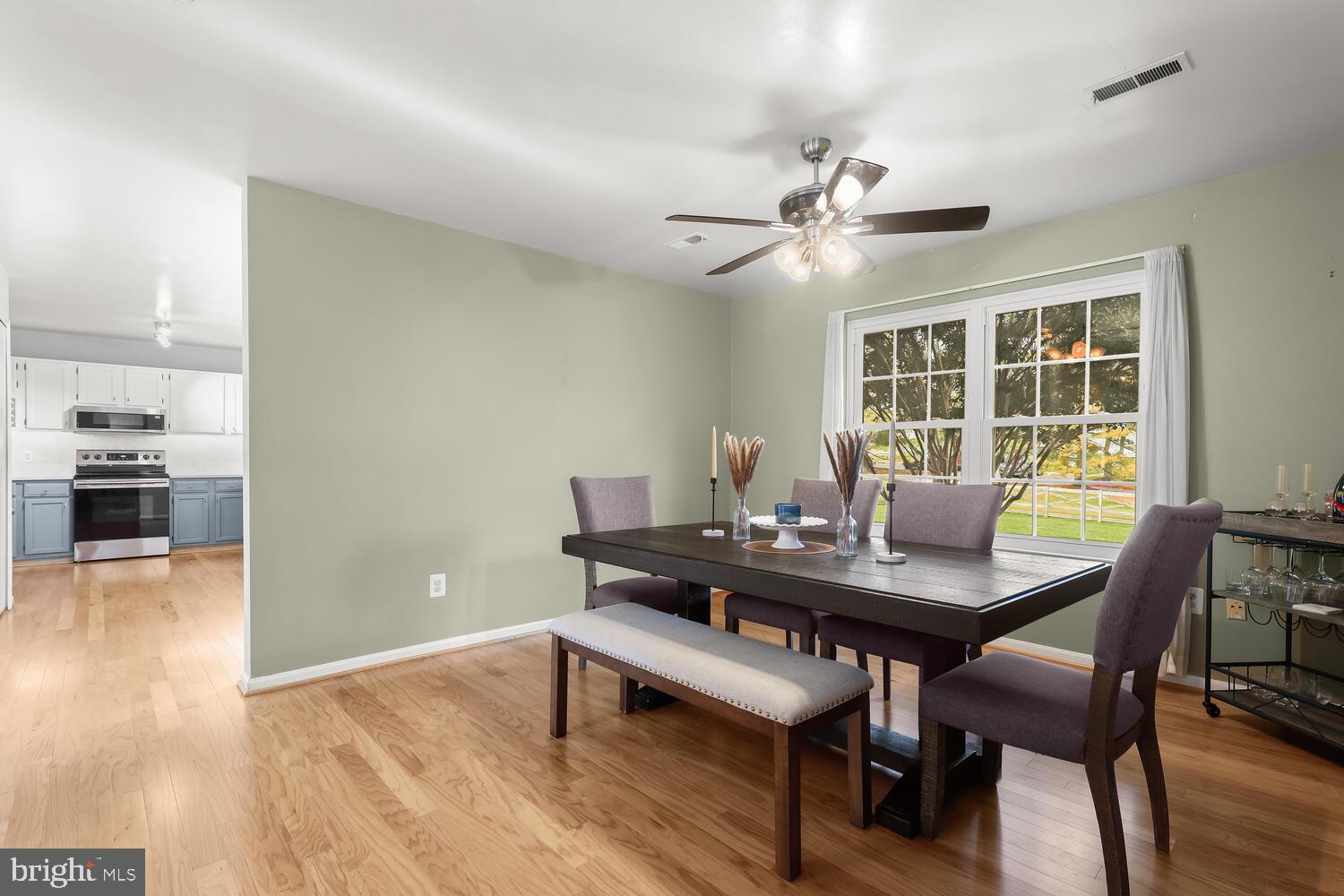 Dining room with a dark wood table, upholstered seating, hardwood floors, and a large window overlooking the yard.