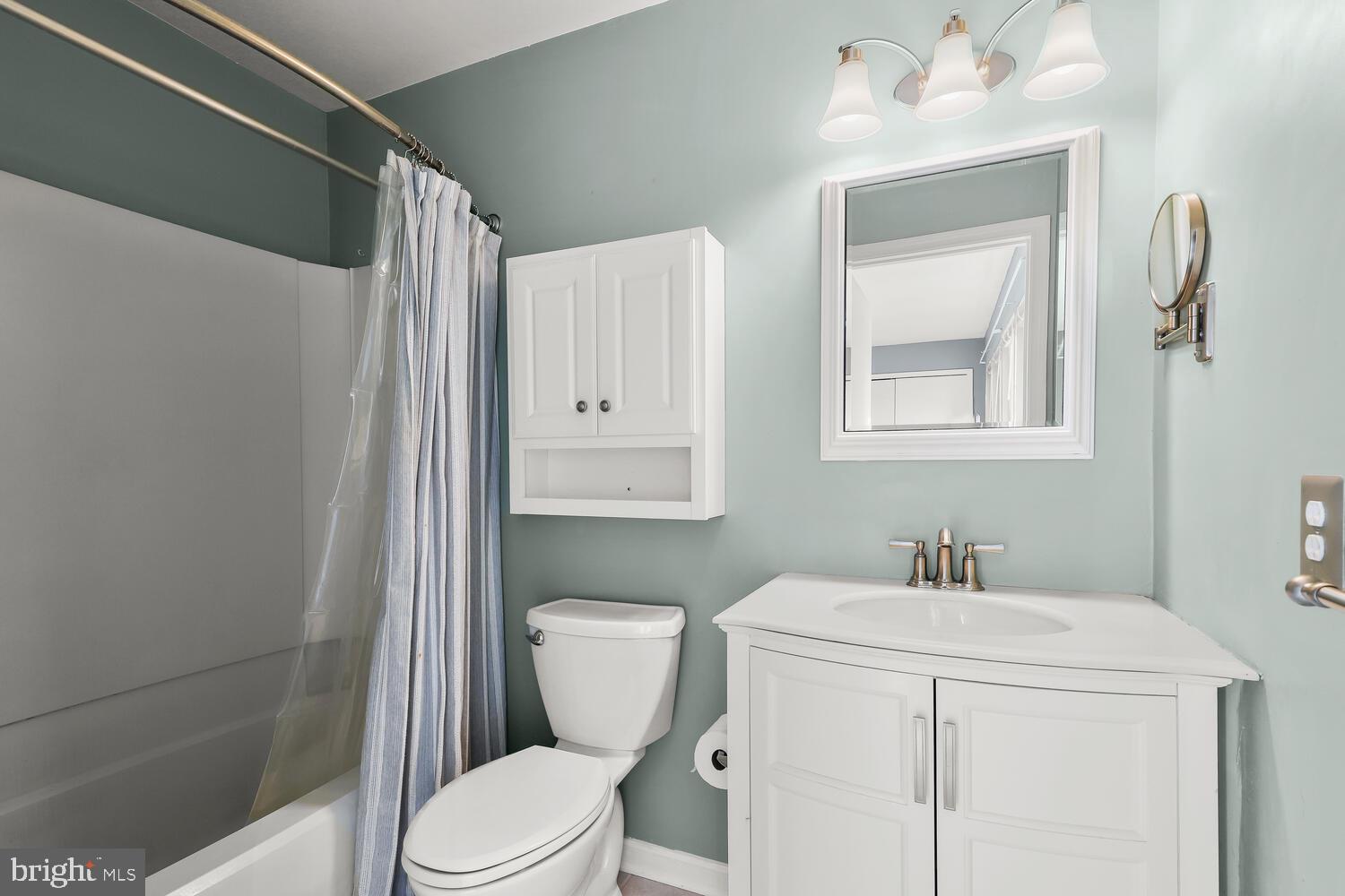 Bathroom with pale green walls, white vanity, framed mirror, and striped shower curtain.
