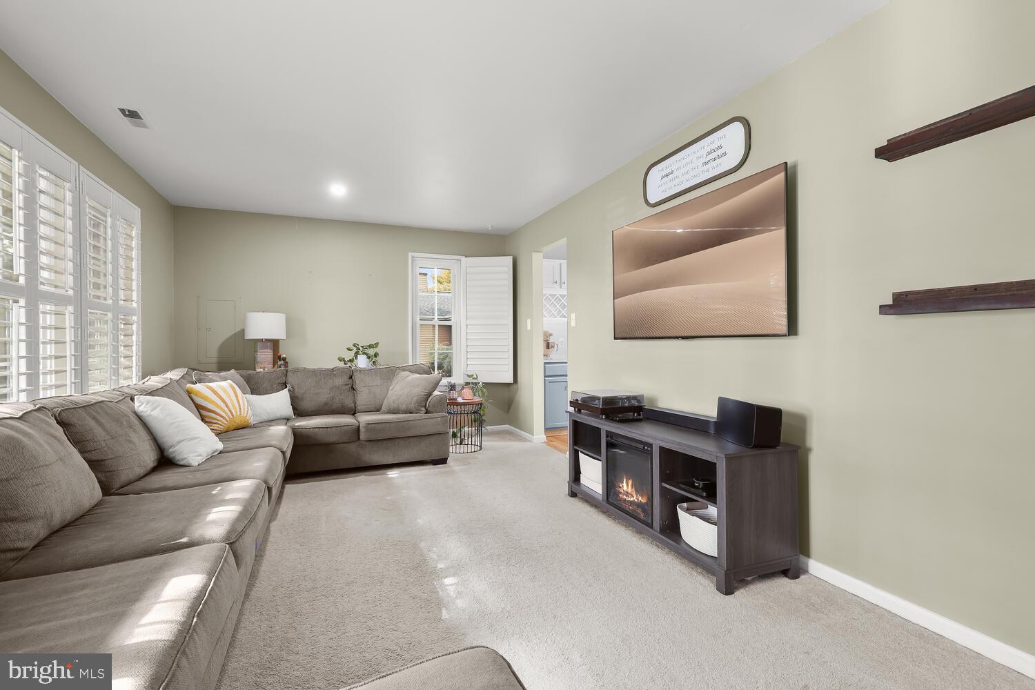 Living room with a gray sectional, plantation shutters, and a TV above an electric fireplace.