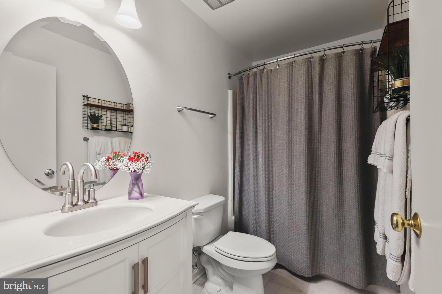 Bathroom with a white vanity, round mirror, toilet, and gray shower curtain.