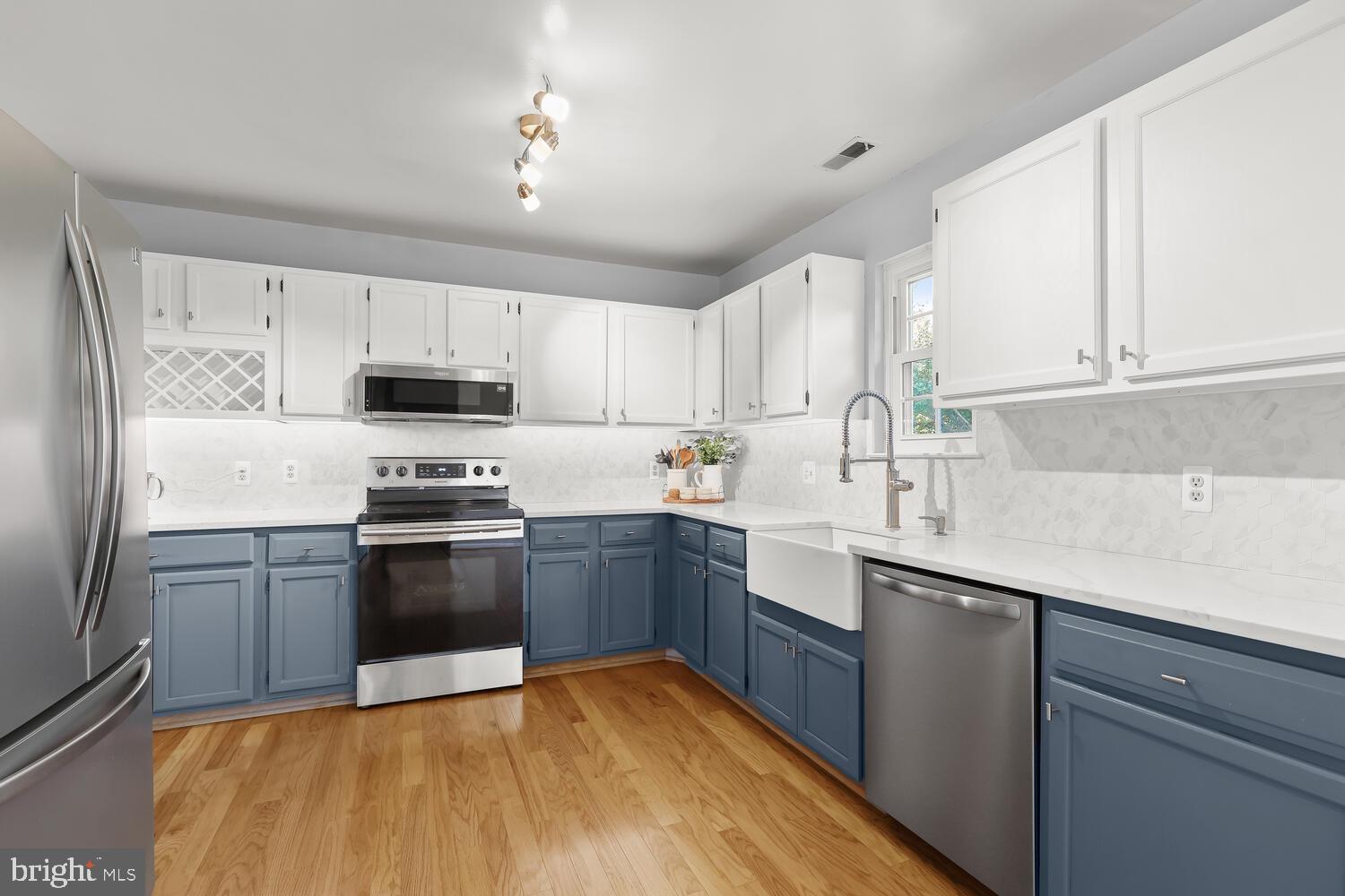 Kitchen with slate-blue lower cabinets, white cabinetry, stainless appliances, and a farmhouse sink.