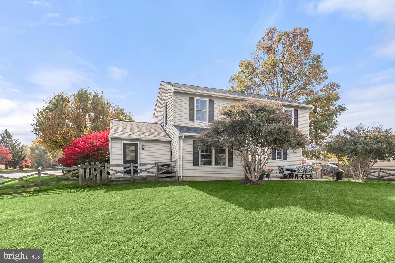 Two-story home with a fenced lawn, autumn trees, and an outdoor dining area.