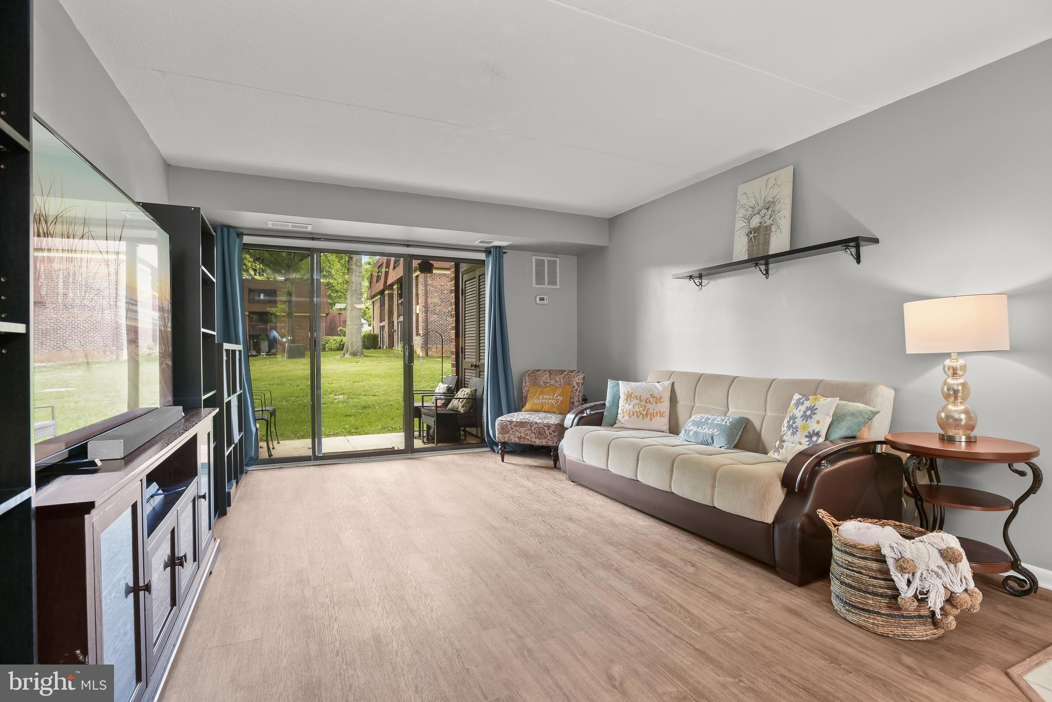 Staged living room with beige sofa and sliding glass doors overlooking a grassy courtyard.