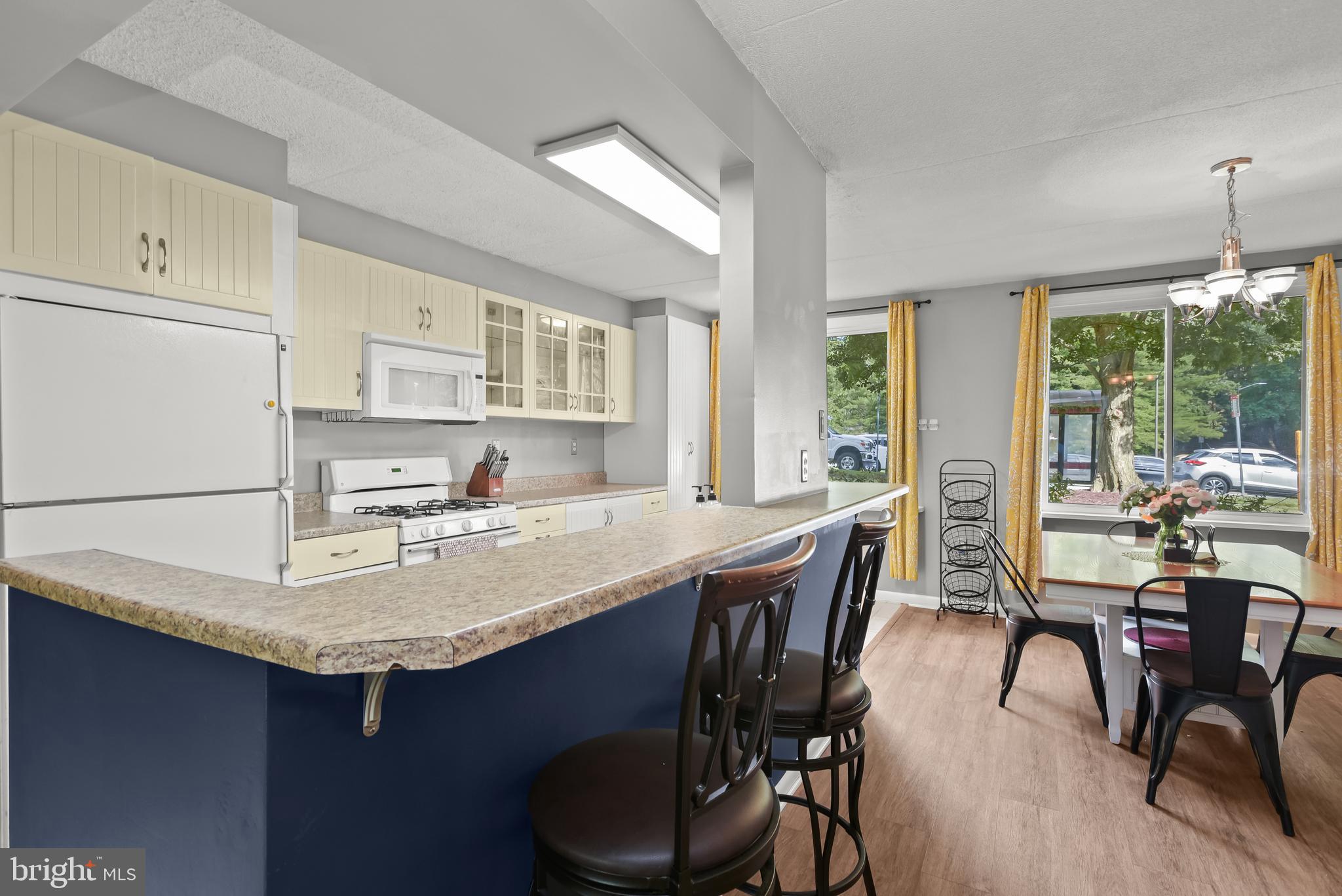 Kitchen and dining area with a long blue breakfast bar, cream cabinets, and large curtained windows.