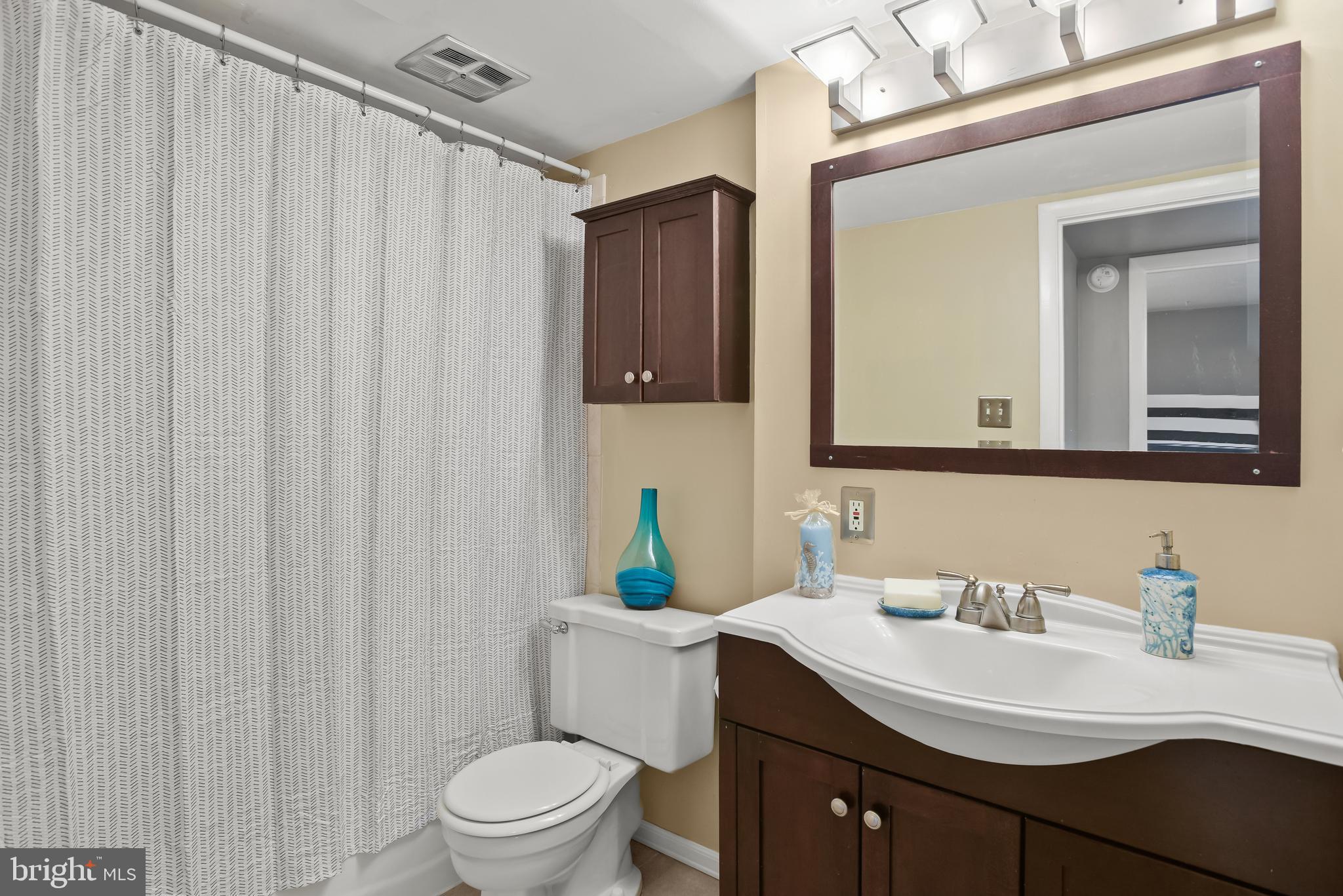 Bathroom with a patterned shower curtain, dark wood vanity, and large framed mirror.