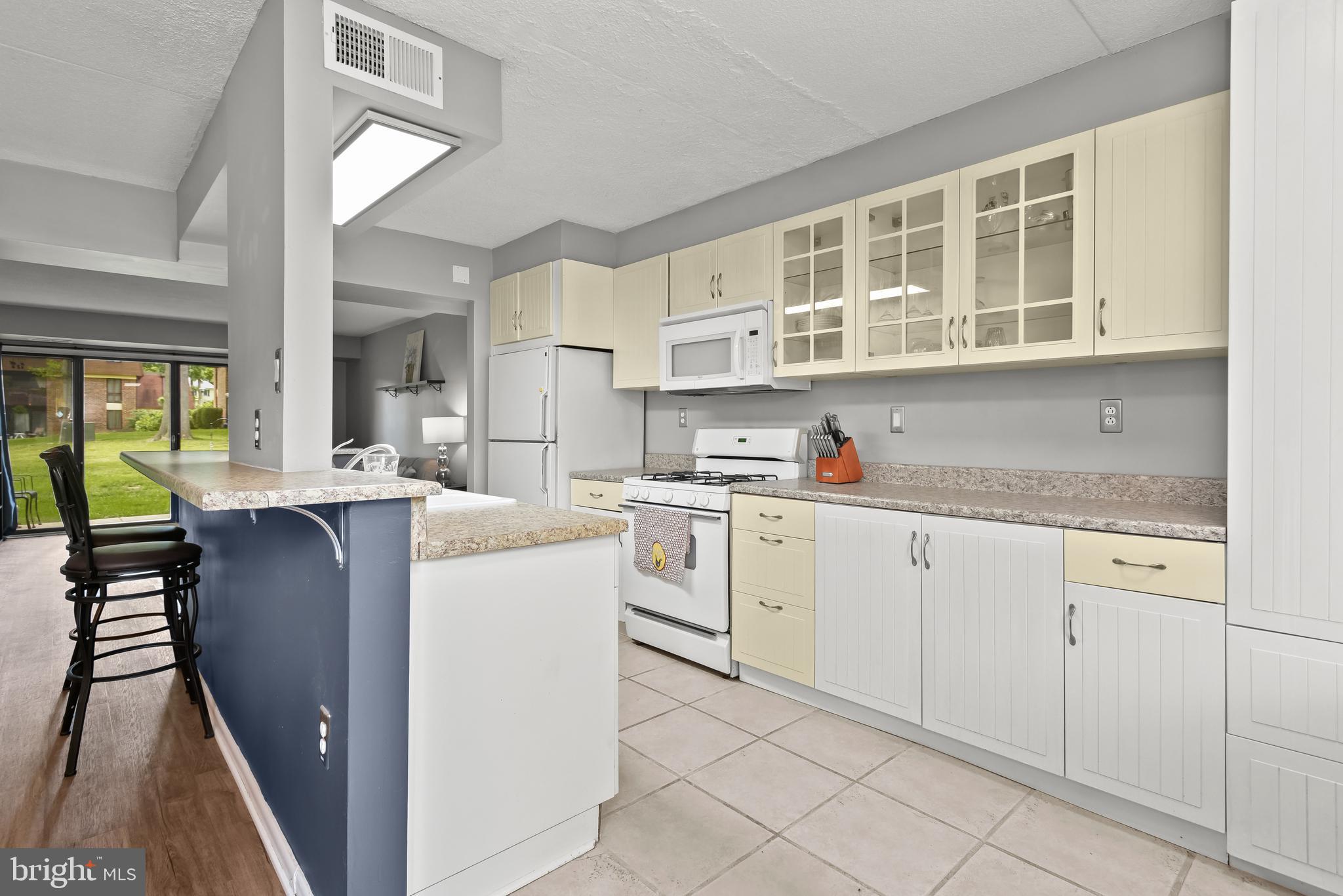 Kitchen with cream cabinets, white appliances, speckled counters, and a blue breakfast bar with stools.