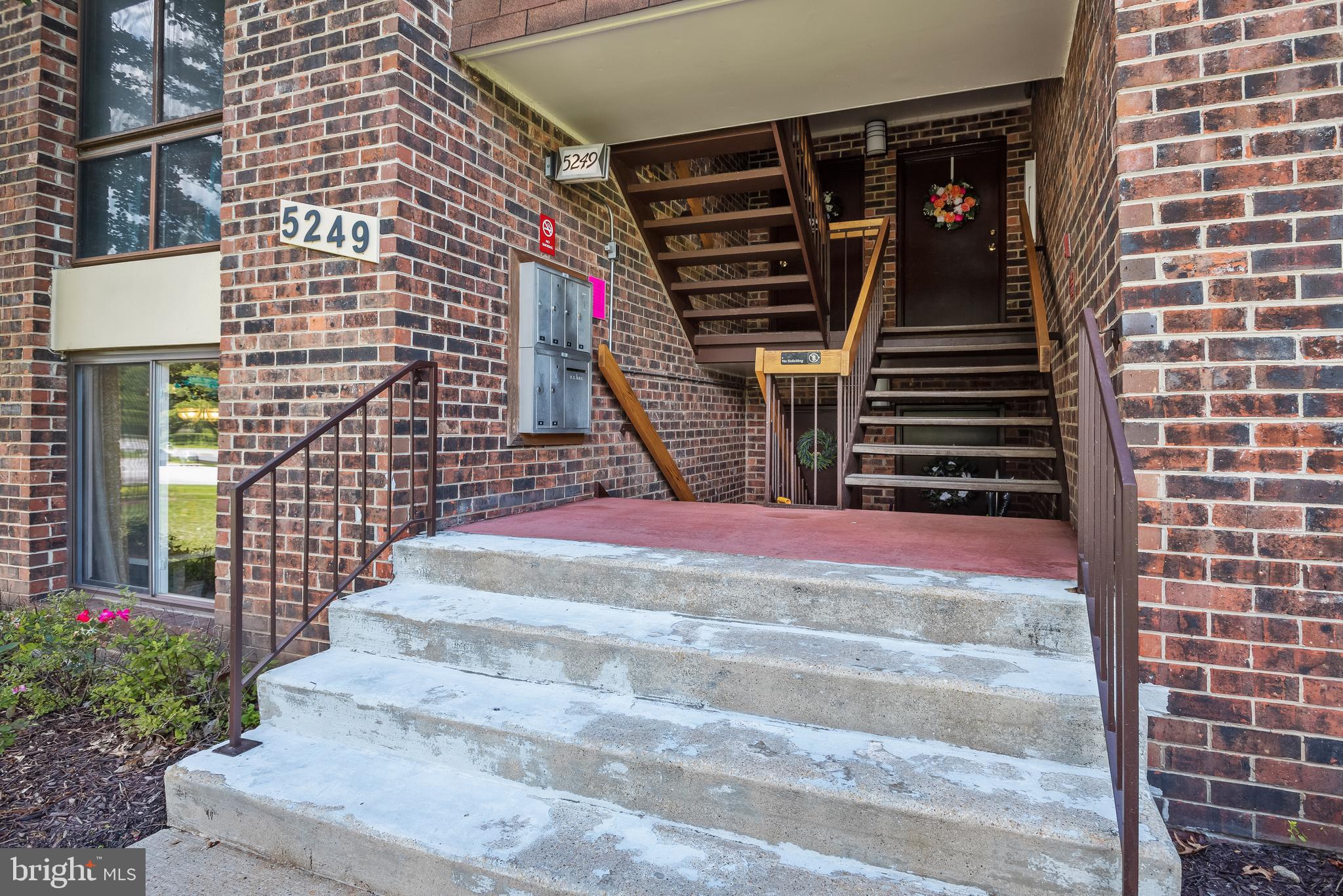 Brick condominium entrance with concrete steps, mailboxes, and an upper-level staircase.