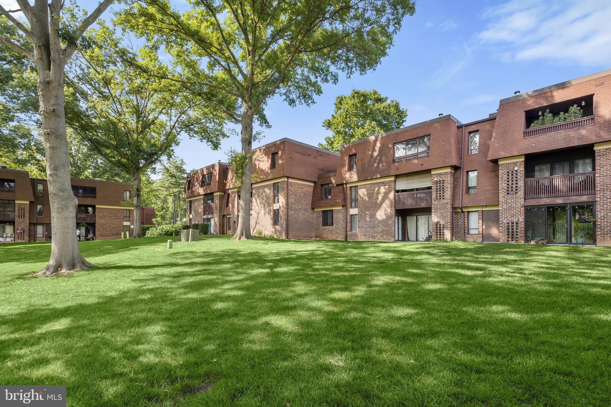 Brick apartment buildings with balconies behind a broad lawn and mature shade trees.