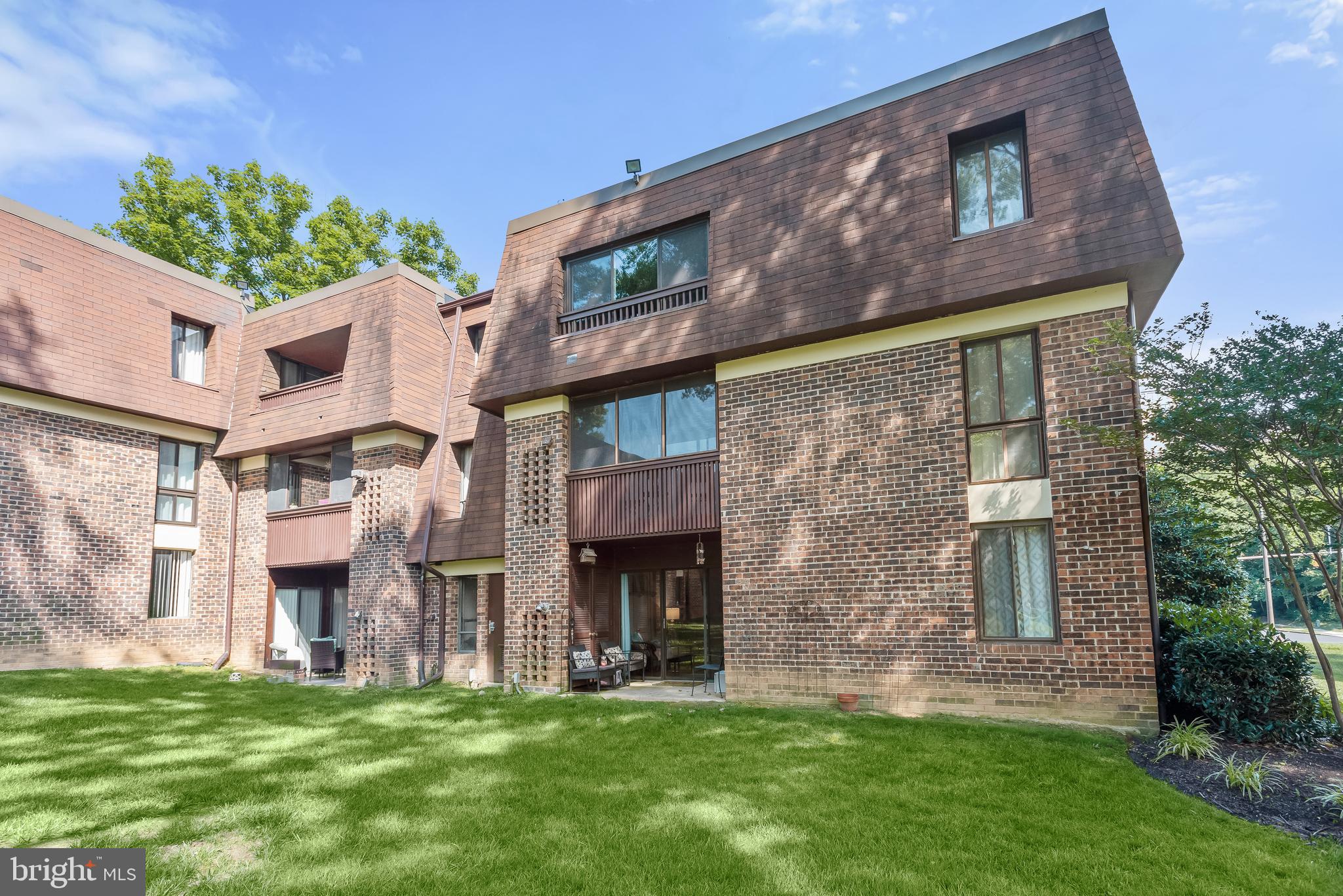 Condominium exterior with brick walls, brown shingle siding, balconies, and a patio beside a lawn.