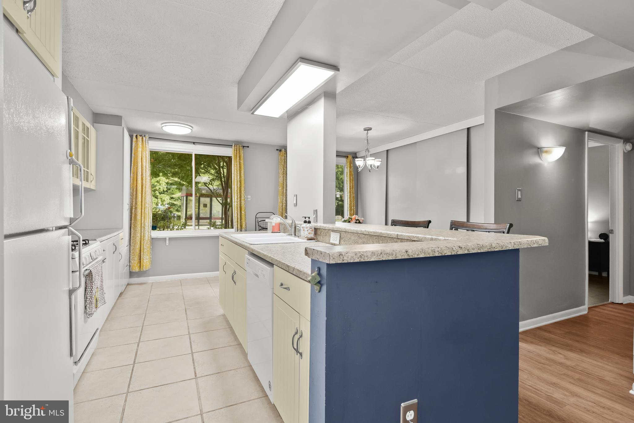 Kitchen with a blue peninsula, stone countertop, cream cabinets, and yellow curtains.