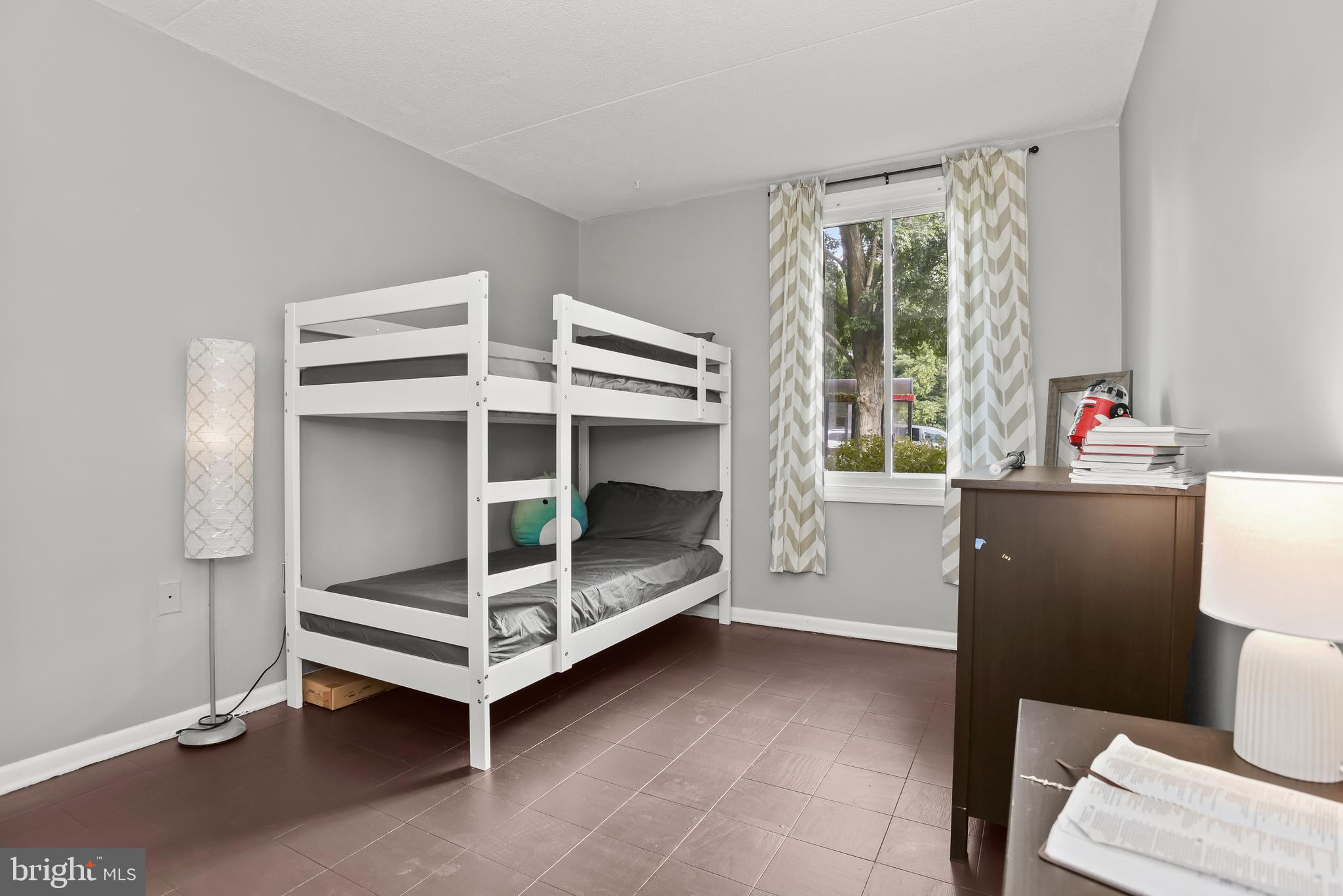 Bedroom with a white bunk bed, gray bedding, patterned curtains, and a window overlooking trees.
