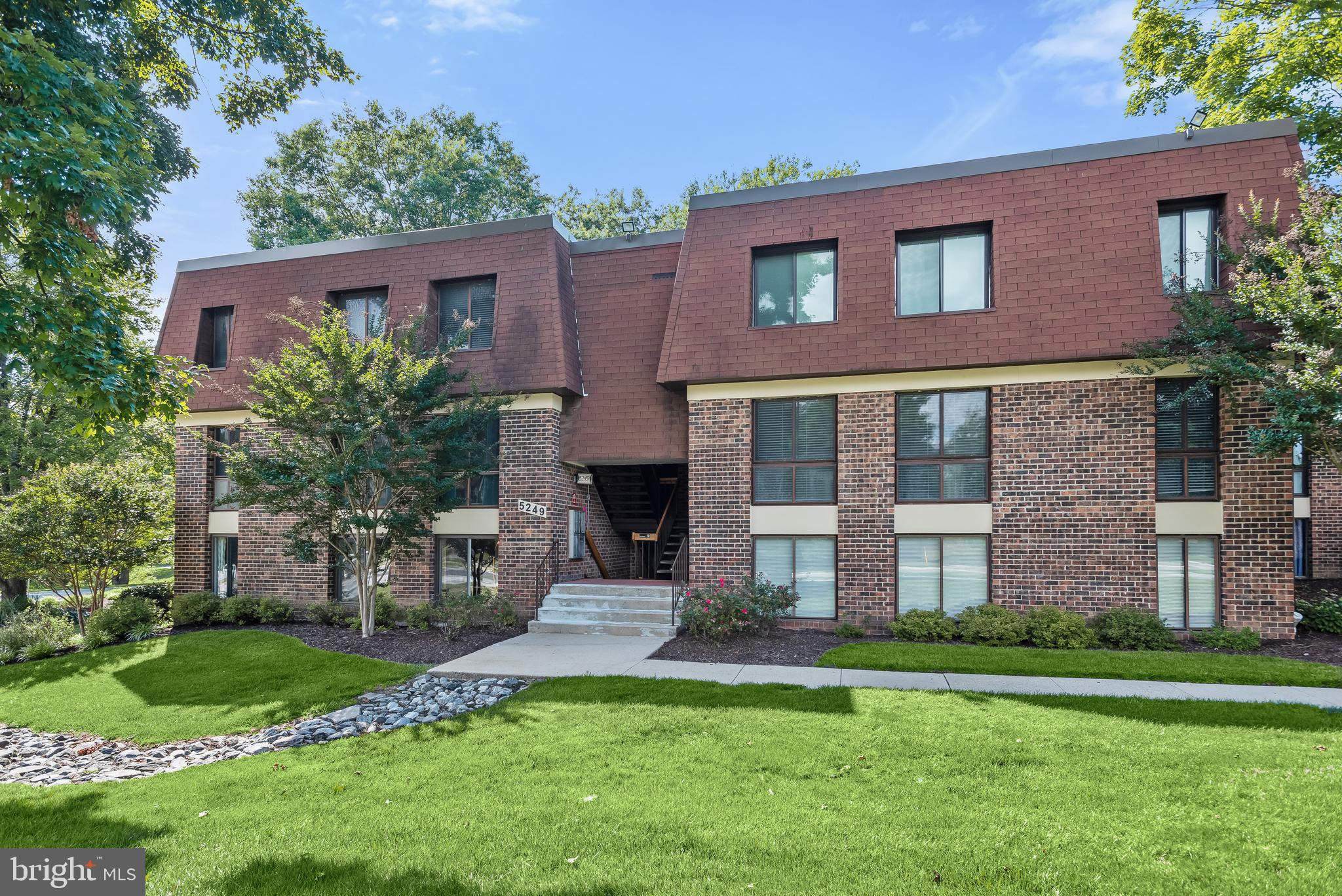 Brick condominium building with a recessed stairway entrance and landscaped lawn.